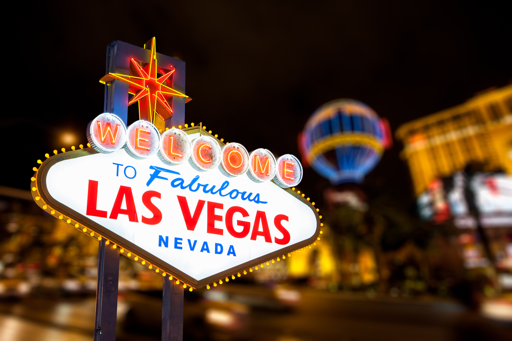 Famoso letrero de bienvenido a Las Vegas con un fondo de la ciudad iluminada de noche.